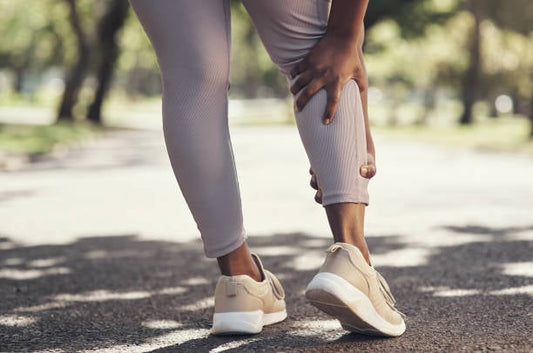 Person holding their leg in pain due to muscle cramp while jogging in a park.