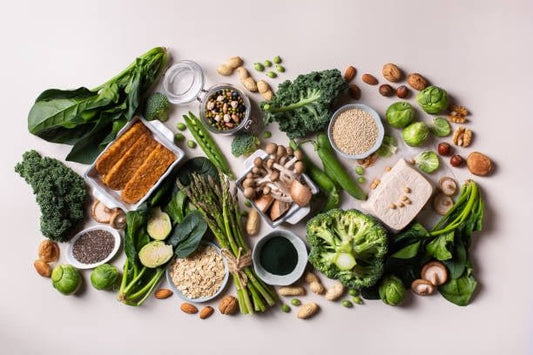 A variety of fresh vegetables, nuts, grains, and legumes arranged artfully on a light background.
