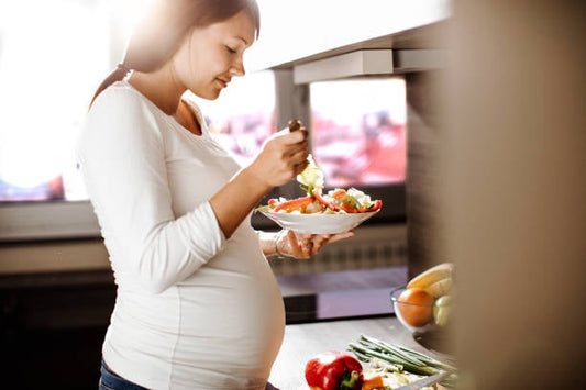 Gravid kvinna äter en hälsosam sallad i köket, viktiga val under graviditeten.