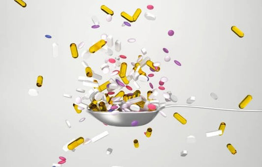 A variety of colorful dietary supplements and vitamins falling from a spoon against a light background.