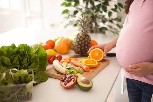 Pregnant woman preparing healthy food with fruits and vegetables on a kitchen countertop to promote a nutritious pregnancy.