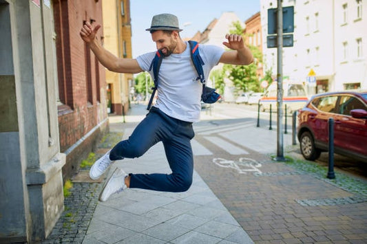 Man in casual outfit jumping joyfully on a sunny city street.