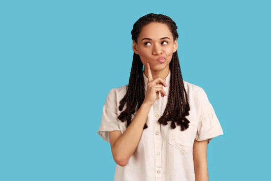 Woman with braids making a thoughtful expression and holding a finger to her lips against a blue background.