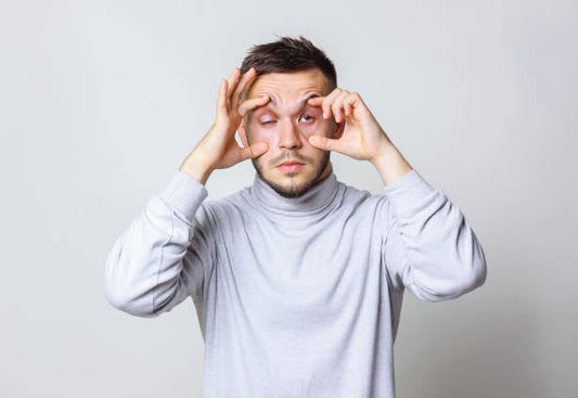 Man expressing fatigue by holding his eyelids while wearing a gray turtleneck sweater.
