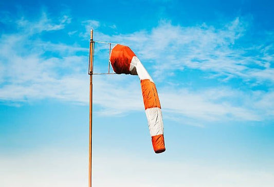 Orange and white windsock flying in a clear blue sky, indicating wind direction and strength.