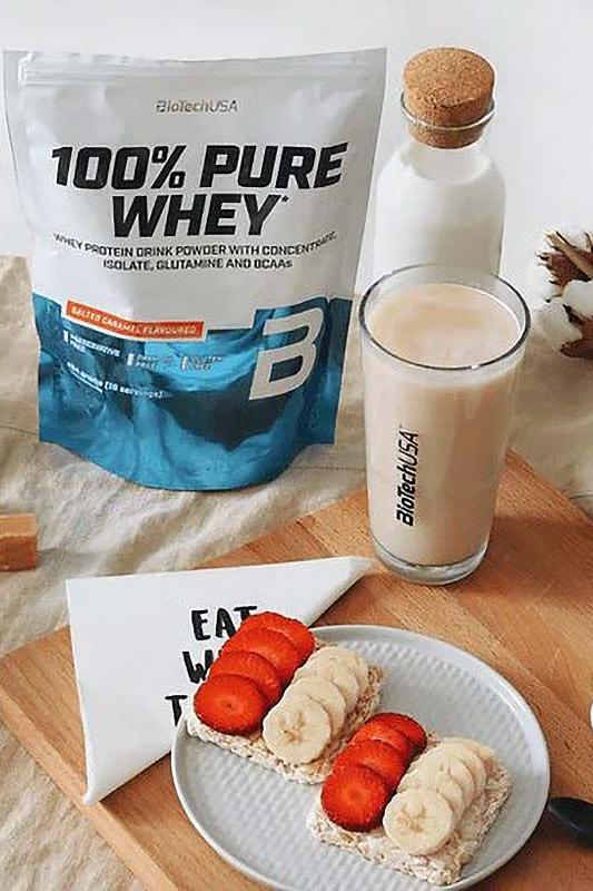 BioTechUSA 100% Pure Whey protein powder with fruit and milk on a wooden table.