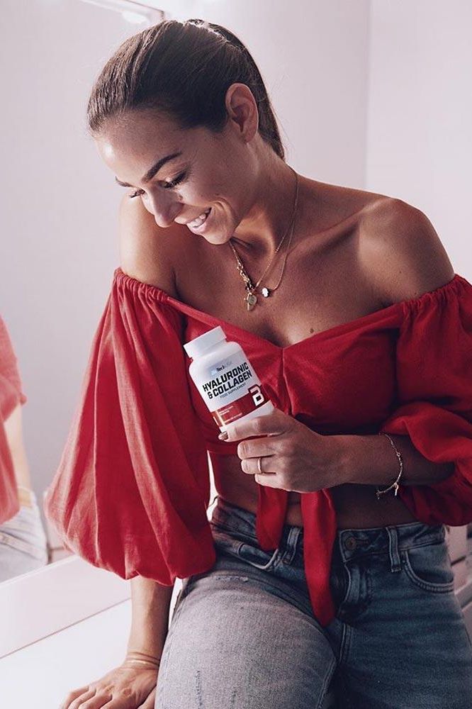 Woman in a red top holding BioTechUSA Hyaluronic & Collagen supplement, showcasing healthy skin and vitality.