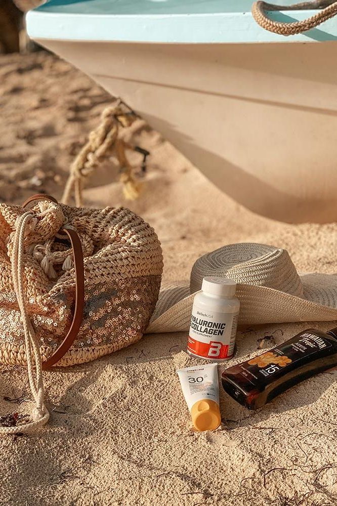 Beach scene with BioTechUSA collagen supplement, sunscreen, and hat on sand next to boat.