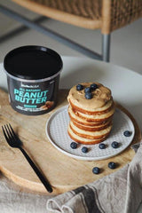 Stack of pancakes topped with peanut butter and blueberries, next to a jar of BioTechUSA All Natural Peanut Butter.