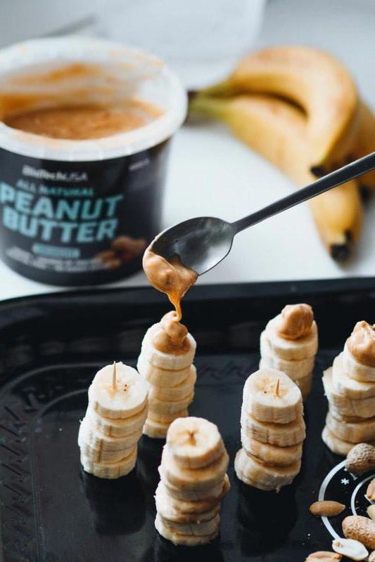 Spoon drizzling BioTechUSA peanut butter over stacked banana slices.