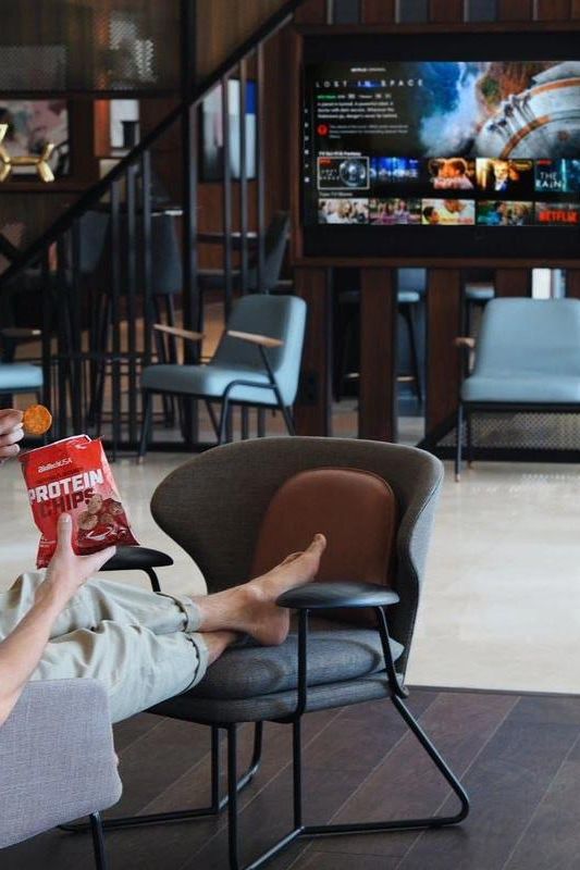 Person enjoying BioTechUSA Protein Chips in paprika flavor while relaxing in a stylish living space.