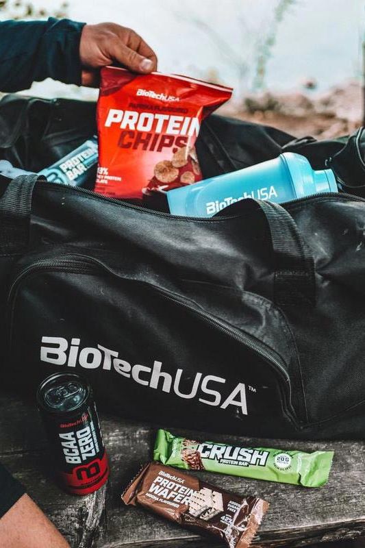 BioTechUSA protein chips in a gym bag among other fitness snacks and beverages.