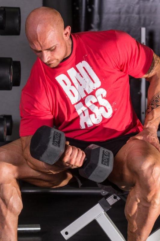 Man lifting dumbbell in red FA Fitness Authority T-Shirt with 'BAD ASS' design, showcasing athletic physique during workout.