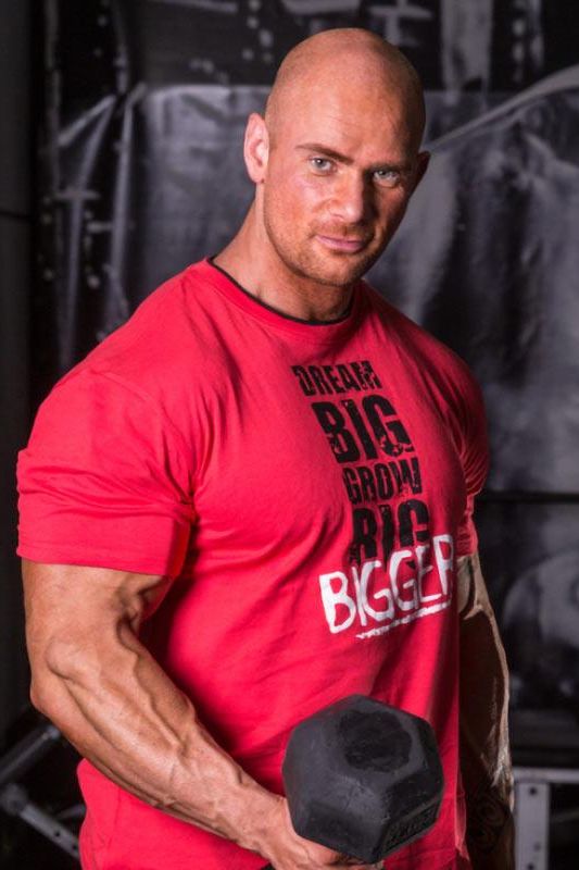 Muscular man holding a dumbbell, wearing a red Fitness Authority T-Shirt, showcasing strength and fitness.