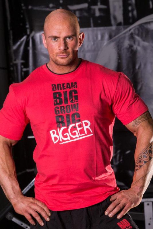 Muscular man wearing a red t-shirt with motivational fitness text, showcasing comfort and flexibility for training.