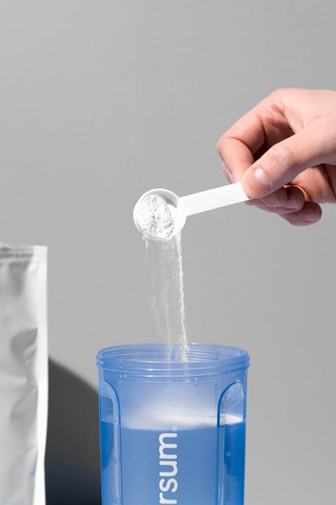 Hand pouring BCAA powder into blue shaker from Nutriversum, showcasing the mixing process.