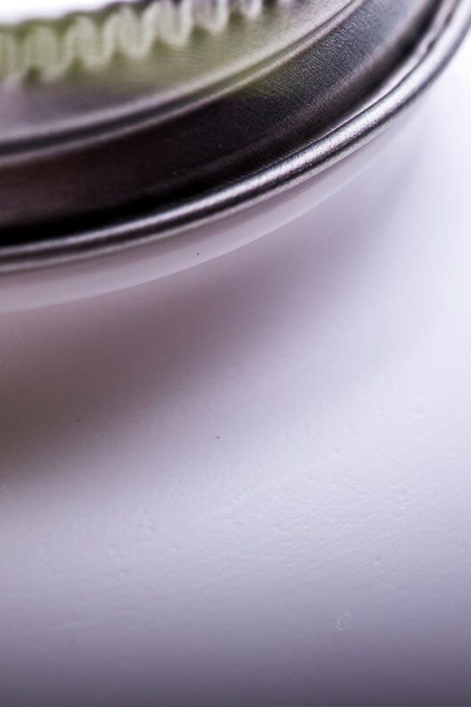 Close-up of a metallic jar lid on a smooth white surface with soft lighting.