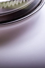 Close-up of a metallic jar lid against a smooth, white surface.