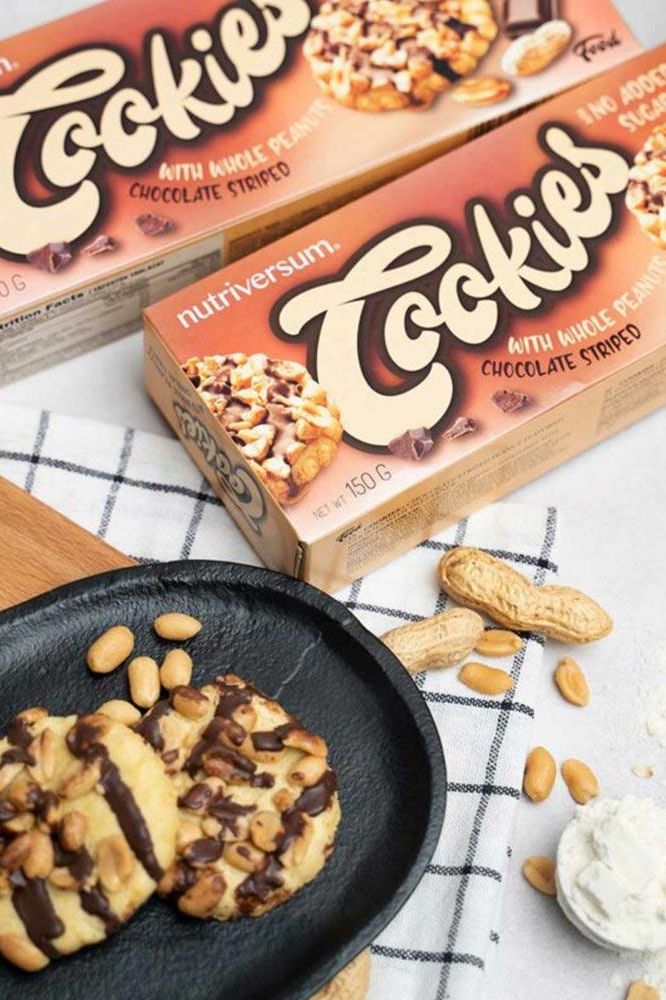 Nutriversum cookies in packaging with whole peanuts, featuring chocolate-striped Peanut Cookies on a black plate.