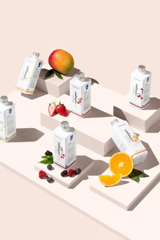 Nutriversum Liquid Collagen bottles displayed with fresh fruits like mango, strawberries, and oranges on a modern pedestal.