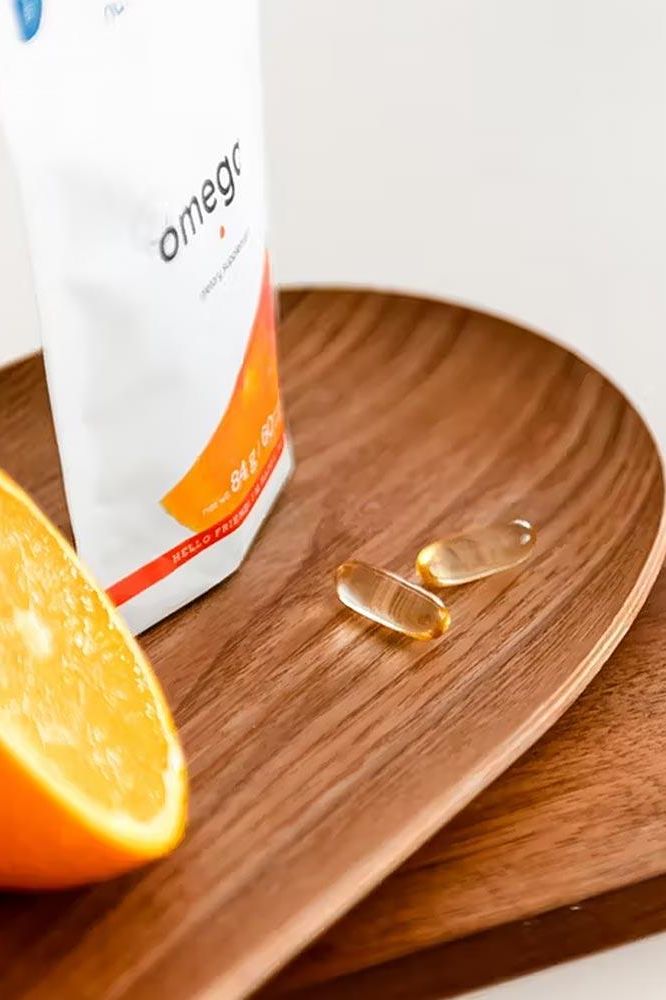 Nutriversum Omega 3 softgels on a wooden plate with an orange slice, showcasing heart health benefits.