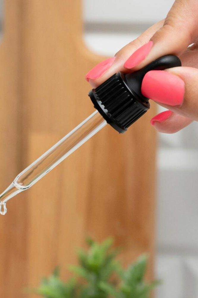 Hand holding a dropper with clear liquid, ideal for dispensing vitamin D+E drops.