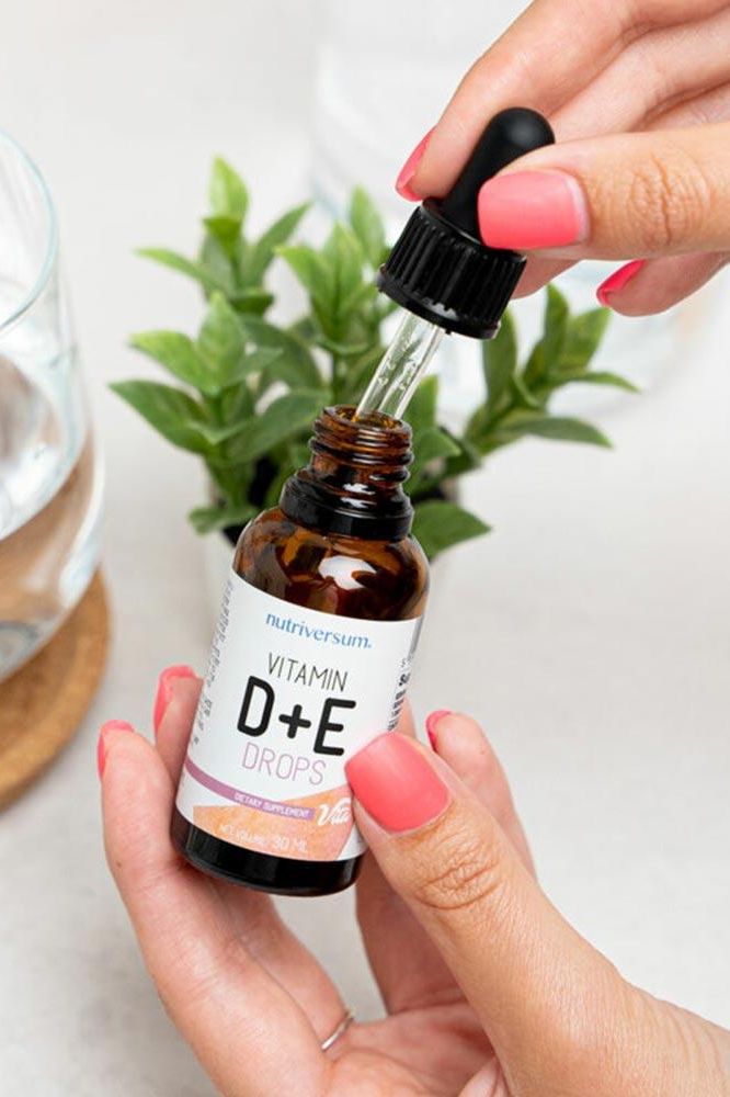 Nutriversum Vitamin D+E drops being held with a dropper, showcasing the unflavored 30 ml product.