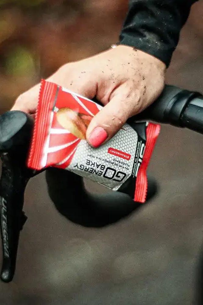 Person holding Science in Sport Go Energy Bake, Strawberry flavor, on a bicycle handlebar.