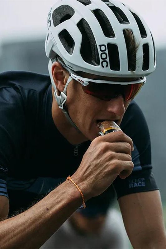 Cyclist wearing a helmet eating a Science in Sport GO Energy Bar Mini during a race, focused on nutrition and performance.