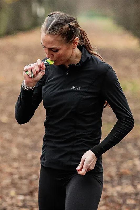 Athlete consuming Science in Sport GO Energy Gel during outdoor training, wearing a black running jacket.