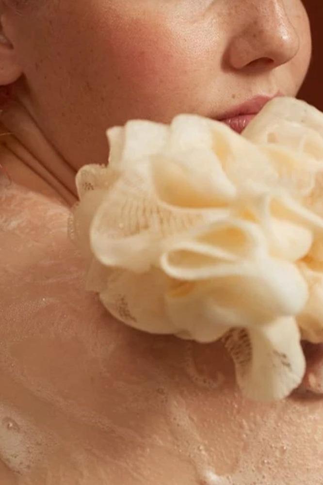 Person holding a soft loofah while enjoying a bubble bath experience.