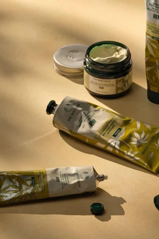 The Body Shop Hemp Vegan Hand Cream and other skincare products arranged artfully on a beige surface.
