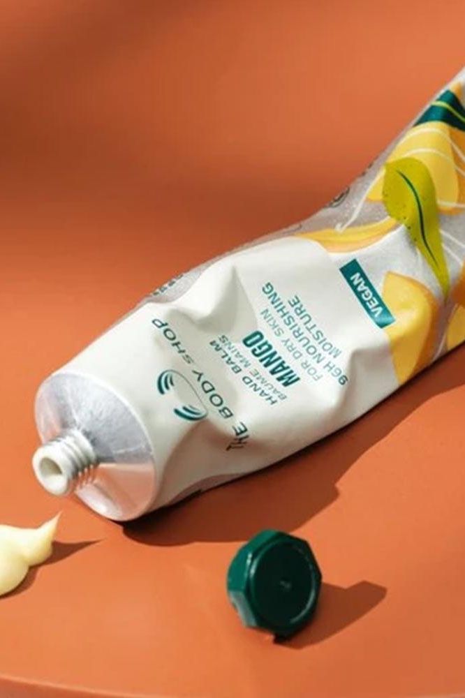 The Body Shop vegan mango hand balm tube on an orange surface.