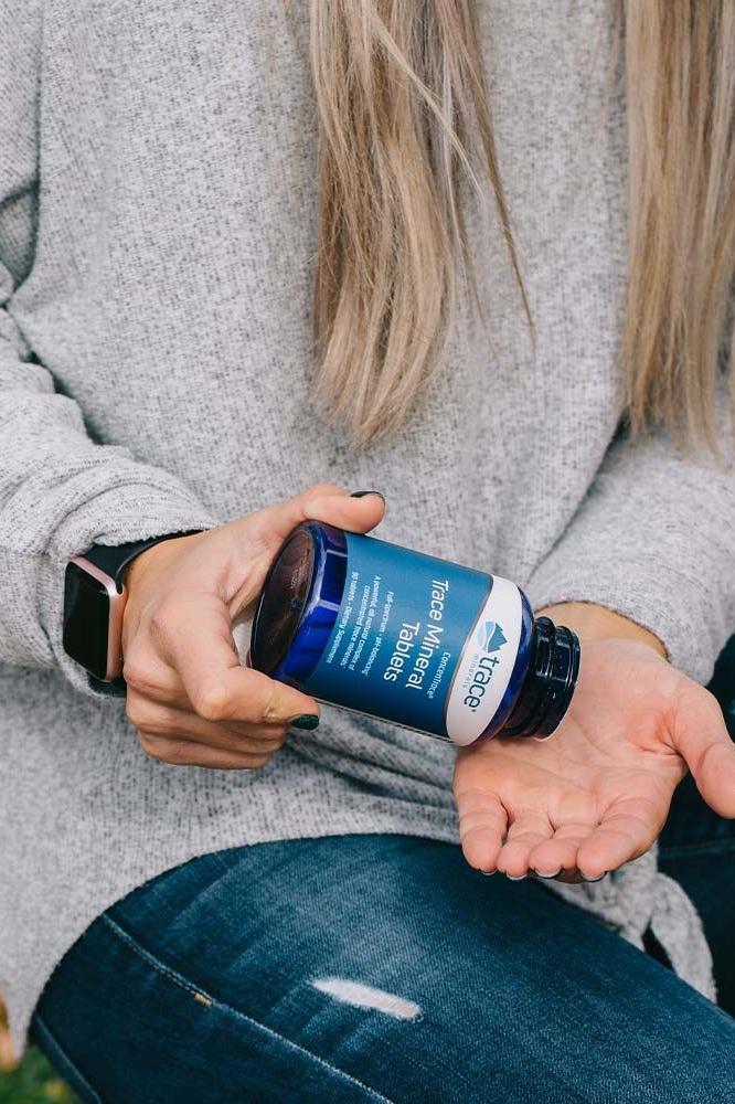 Woman holding ConcenTrace Trace Mineral Tablets bottle, ready to take the natural health supplement.