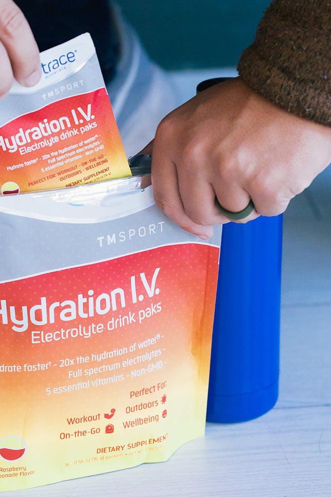 Person reaching for Trace Minerals Hydration I.V. Electrolyte Drink Paks to add to a blue water bottle.