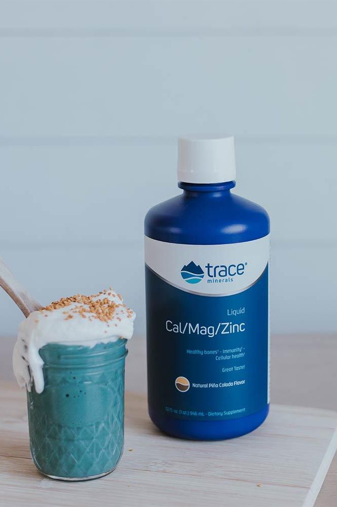 Trace Minerals Liquid Cal/Mag/Zinc in a blue bottle beside a green smoothie topped with cream.