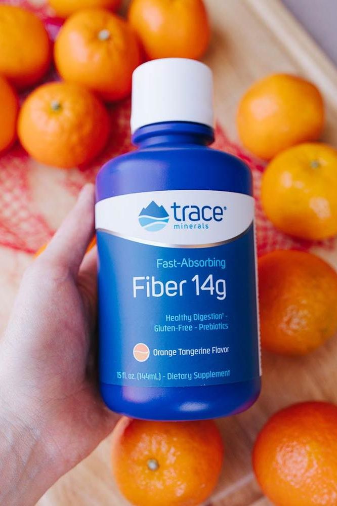 Trace Minerals Liquid Fiber 14g supplement bottle in hand with tangerines, supporting digestion and weight loss.