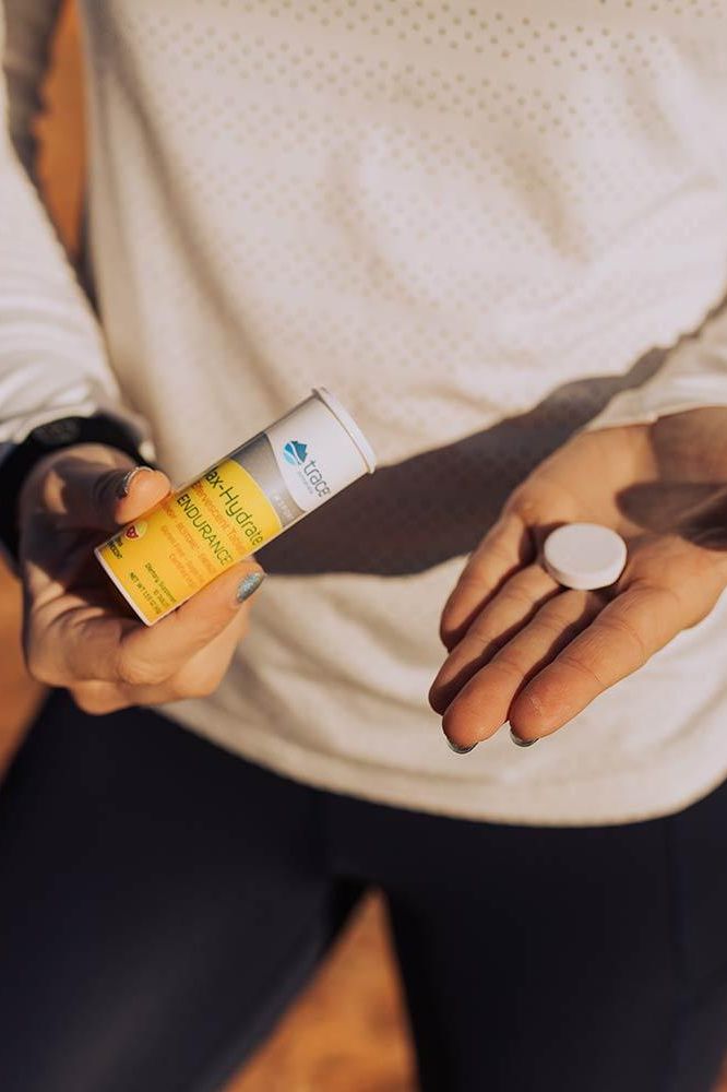 Person holding Trace Minerals Max-Hydrate Effervescent Tablet tube and a tablet, showcasing hydration support.