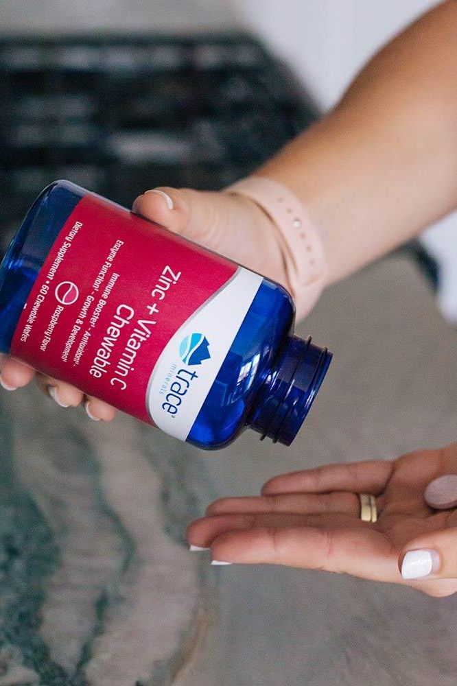 Trace Minerals Zinc + Vitamin C Chewables in a blue bottle being poured into a hand.
