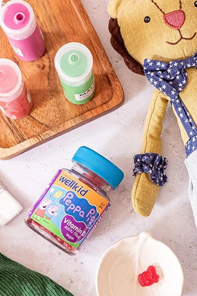 Wellkid Peppa Pig Vitamin D gummies with colorful jars and a stuffed lion in a playful arrangement.