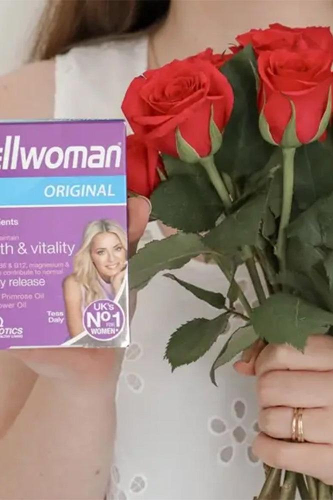 Woman holding Vitabiotics Wellwoman Original multivitamin box and red roses, promoting health and vitality for women.